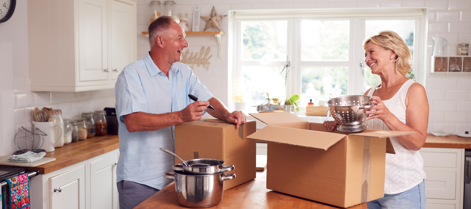 Two people pack up belongings in their kitchen. Downsizing Tips.